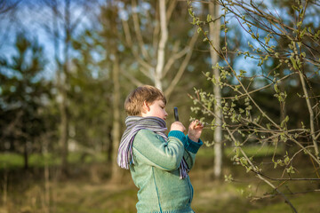 A funny boy walks through the spring park, examines the leaves with a large magnifying glass, looks...
