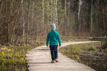 A boy walks along a path in a green park. The path is a bridge over the lake.