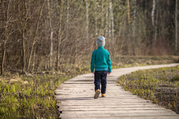 A boy walks along a path in a green park. The path is a bridge over the lake.