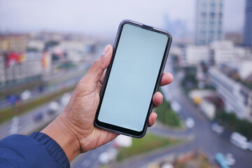 young man hand using smart phone with green screen against city buildings 