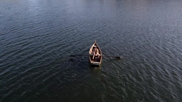 A lonely man oaring the boat at middle of lake.