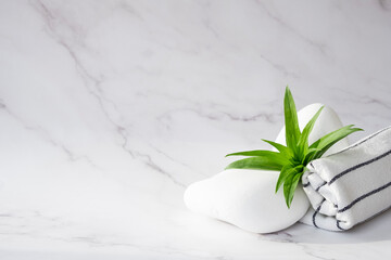 SPA background concept. White stones, towel, and leaves of green plant on marble background with copy space. Relaxation, body care and beauty treatment concept.