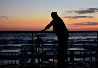 mężczyzna o zachodzie słońca nad morzem, man at sunset by the sea, pensive man leaning against a railing overlooking the seascape and sunset
