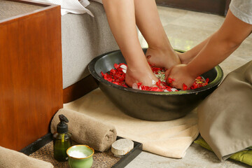 Feet massage in spa salon. Woman feet dipped in a wooden bowl with water petals, a day at the spa, massage, pedicure and beauty treatment	