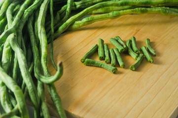 A bunch of long beans and long beans cut into short pieces on a wooden cutting board isolated on a white background