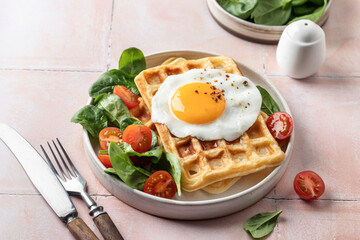 Savory waffles, fried egg and spinach, cherry tomato salad. Delicious healthy breakfast on pink tile background