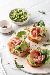 Bruschetta with ham or prosciutto, cream cheese, cucumber, spinach and microgreens. Tasty sandwich or toasted bread on white tray. Tasty appetizer or breakfast