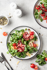 Green salad with ham or prosciutto, corn salad leaves, tomatoes and cheese. Healthy diet lunch on white marble background top view flat lay