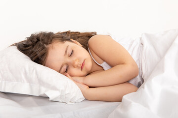 Fototapeta premium Cute little girl sleeping in bed. Little brunette girl sleeps sweetly in bed with white linen. space for text. healthy baby's sleep