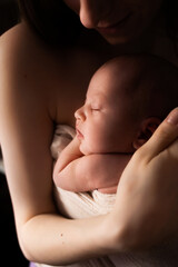 gentle close-up portrait of a newborn baby in the arms of mom in the background. photograph in a dark key, dark color. a happy family.  a happy family
