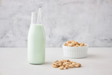 Pistachio milk in a bottle on a gray table next to pistachios. Vegetable milk. Nut milk for vegans