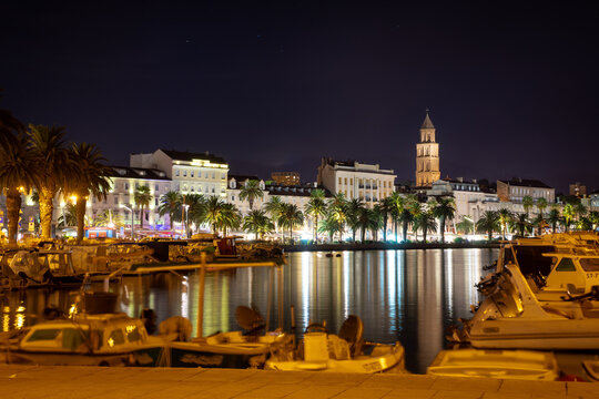 Riva boardwalk in Split, Croatia at night. Reflections of colorful city lights in the water.