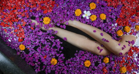 Young woman takes a bath in the tub full of petals, legs close up, spa weekend, wellbeing, body care and beauty concept	 - Powered by Adobe