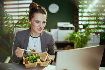 happy 40 years old woman employee in green office eating salad