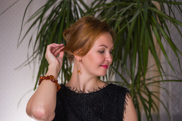 a woman with red hair, an amber bracelet on her arm and a black dress. the background is a tropical palm tree.