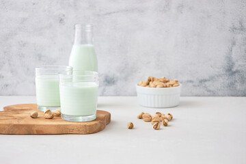 Glasses of homemade pistachio milk on a wooden board next to pistachios. The perfect drink for vegans
