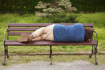 Drunk adult man, drunkard, alcoholic sleeps in the park outdoors on a wooden bench. Photography, portrait, lifestyle.