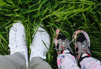 A man and a girl, a child, a daughter and a father in sports leather sneakers are standing on the grass, walking, outdoor recreation. Photography, close-up portrait, top view, leisure, sports.