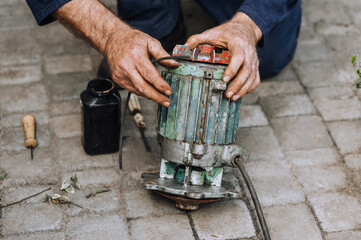 Male professional, electrician, electromechanic repairing an old rusty electric motor in a...