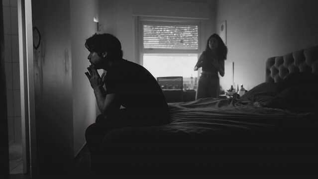 Relationship break-up: Couple fighting and arguing. Depressed man covering face in frustration while female partner screams at him in bedroom. Monochromatic dramatic black and white