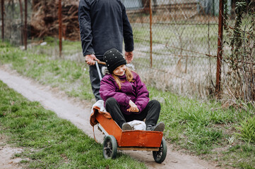 A strong man, father, grandfather rides, carries on a rusty old cart, wagon along the road in the village, countryside, a small smiling, happy girl, a child. Photography, portrait, emotions.