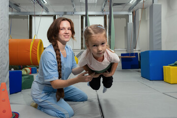 Child with physiotherapist on swing during sensory integration session. Little girl in...