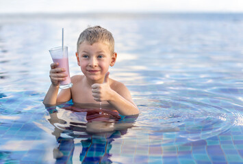 A little boy in the swimming pool drinks a milkshake.