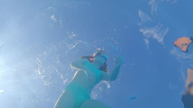 a kid girl wearing swimming goggles dives in the pool and takes a picture of himself.
