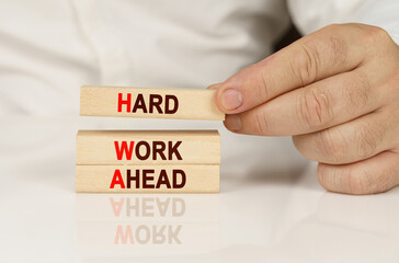 In the hands of a person and on a reflective surface are wooden blocks with the inscription - Hard Work Ahead