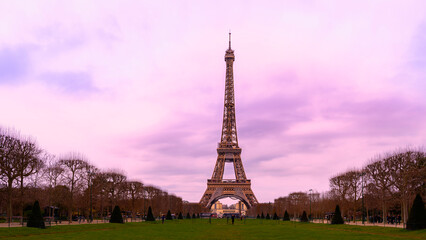 The Eiffel Tower over the green lawn field of Champ de Mars, Field of Mars, in Paris, France, an overcast sunset landscape