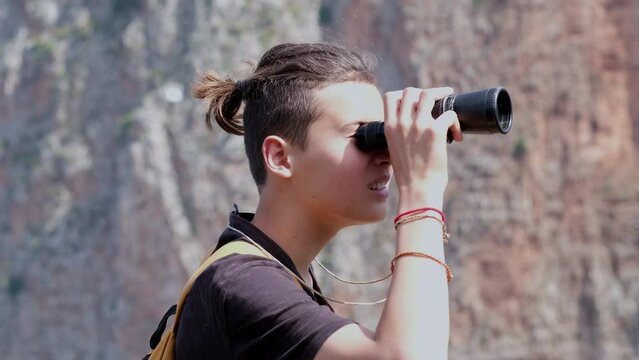 Tourist boy looking through binoculars in beautiful mountains while hiking with family. Inquisitive boy looking through monocular monocle during a school trip to mountains.