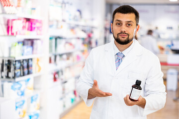 Friendly young adult male pharmacist standing at drugstore with medical product in hands