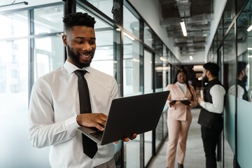 Young african american man in business suit holding laptop while standing at office corridor