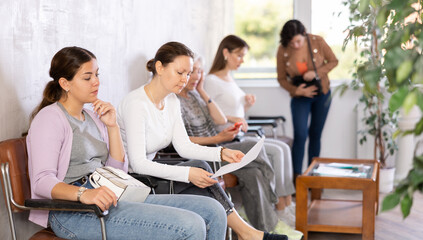Fototapeta premium Young focused woman in casual clothes waiting for her turn while sitting on chair in reception..