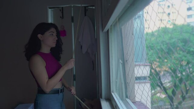 Woman shutting window blinds at home. Person turning room pitch dark