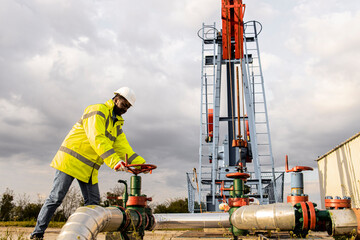 Oil field worker closing industrial valve by the oil rig controlling production.