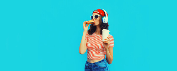 Portrait of young woman listening to music in headphones with burger fast food and cup of coffee or...