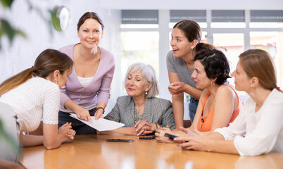 Smiling interested woman conducting informal work meeting with mixed age group of female colleagues...