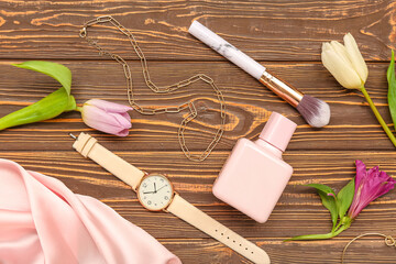 Composition with bottle of perfume, female accessories, makeup brush and flowers on wooden background