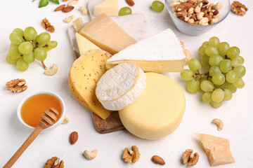 Board with different types of tasty cheese, grapes and honey on light background