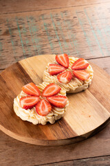 dessert of two waffles with white chocolate cream on a round wooden board and cut strawberries on a wooden table.at an angle from above