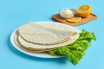 Plate of thin lavash with lettuce on blue background