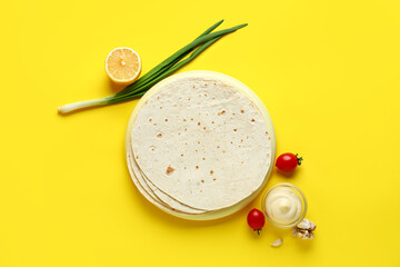 Board with thin lavash, tomatoes and sauce on yellow background