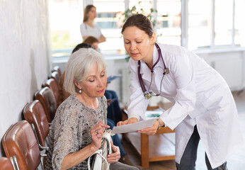 in waiting room of medical clinic, girl doctor interprets results of tests to surprised, annoyed female senior patient. Medical tourism