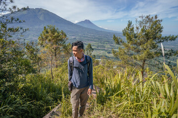 Naklejka premium Young man Indonesian hiking mountain through the forest and foot path. The photo is suitable to use for adventure content media, nature poster and forest background.