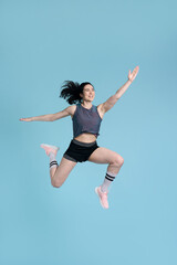 Fototapeta na wymiar Portrait beautiful smiling woman wearing sportswear jumping high looking away, isolated on blue background. Successful professional runner, athlete training, doing exercises . Sport, healthy lifestyle