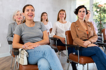 Young positive woman in casual clothes listens to lecture while sitting on chair in office