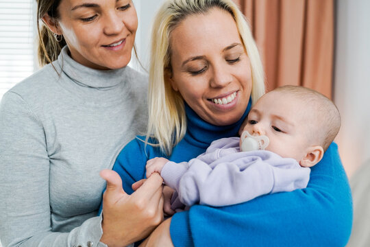 Gay lesbian couple and newborn baby having tener moment indoors at home - Lgbt family concept - Focus on right mother face