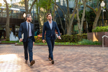 Businessmen go to work. Business taliking. Two businessmen in elegant business suits, walking and talking in city street. Colleagues and friends. Two cheerful business men walking outdoors.