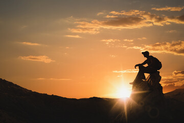 Silhouette of man with backpack sitting on peak in mountains at sunset. Space for text